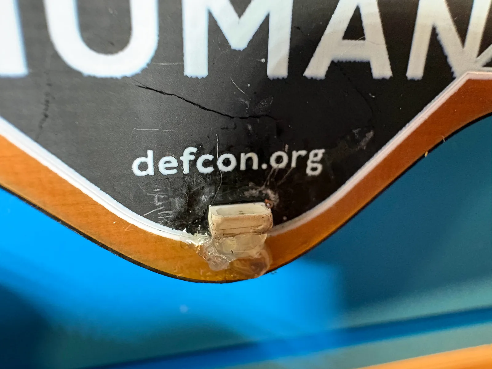 Side view of the repaired LED and its hot glue on the badge edge, below the word HUMAN.