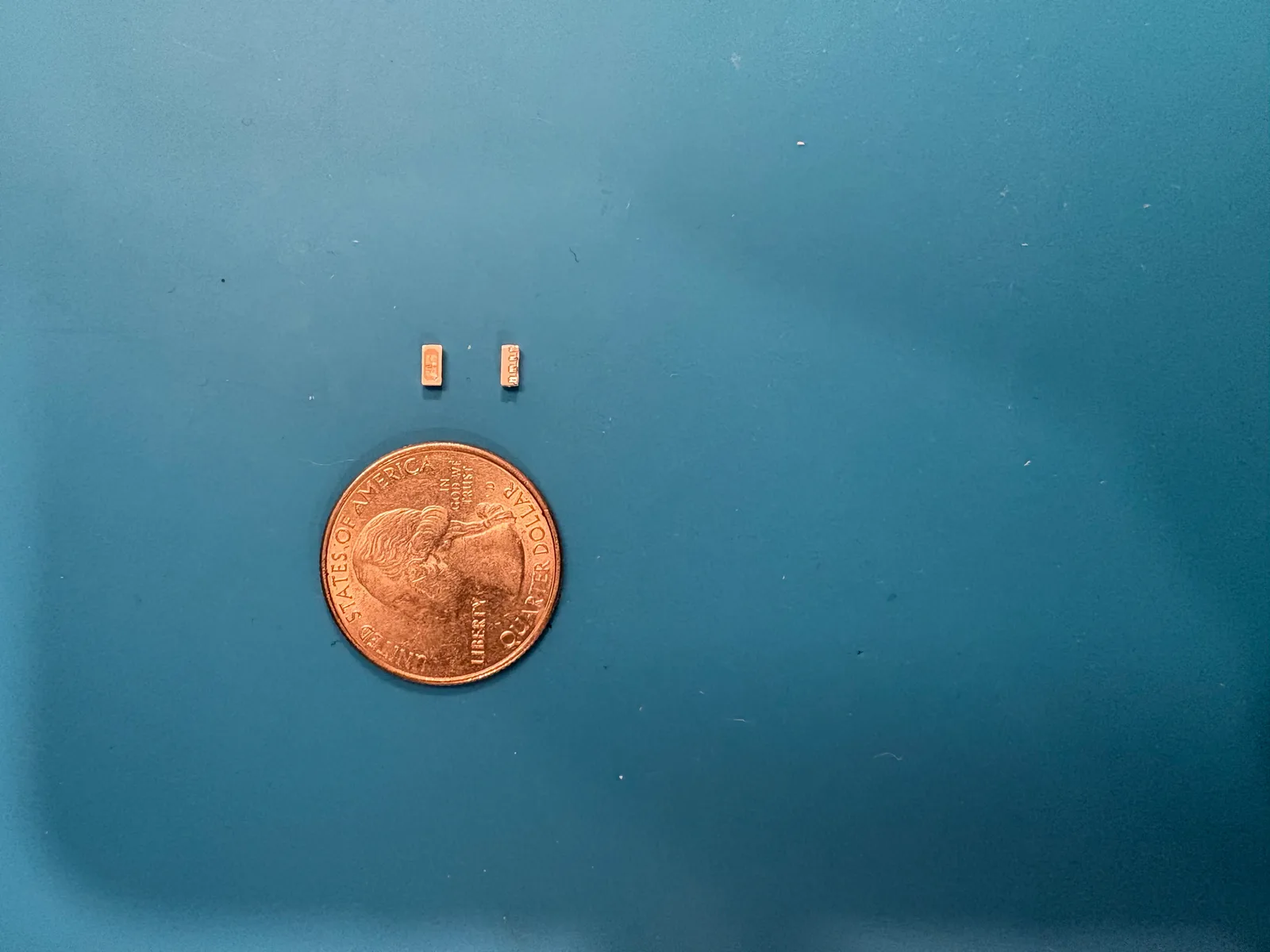 Two SK6812SIDE LEDs on a desk mat next to a quarter, which dwarfs them.